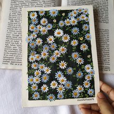 an open book with white and yellow daisies in the middle is being held by a hand