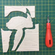 cut out pieces of white paper next to a pair of red handled pliers on a green cutting mat