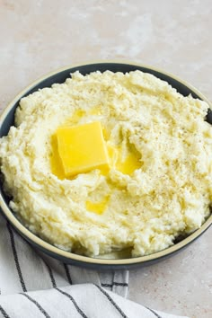 a bowl filled with mashed potatoes and butter on top of a striped towel next to a knife