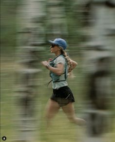 a blurry photo of a woman running through the woods in shorts and a hat