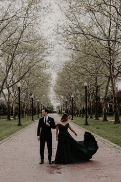 a man and woman in formal wear walking down a brick path with trees lining both sides