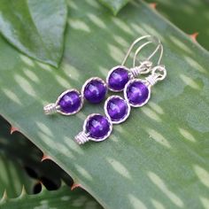 "Three juicy purple 6mm amethyst beads, stacked and outlined with sterling silver wire. This glowing purple shade is one of the hottest colors for the season, and these elegant dangles are sure to get noticed! They measure 1-5/8\" long including the sterling silver kidney earwires. Amethyst is the birthstone for February. Can also be made with 14kt gold filled wire." Hypoallergenic Purple Beaded Earrings, Nickel-free Purple Beaded Earrings With Round Beads, Nickel-free Purple Beaded Earrings, Elegant Purple Wire Wrapped Jewelry, Hypoallergenic Purple Round Bead Earrings, Adjustable Hypoallergenic Purple Beaded Earrings, Nickel-free Purple Sterling Silver Beaded Earrings, Purple Wire Wrapped Drop Earrings, Adjustable Wire Wrapped Purple Beaded Earrings