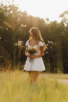 a beautiful young woman holding a bouquet of flowers in her hands walking through tall grass