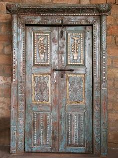 an old wooden door with decorative carvings on the front and side panels, against a brick wall