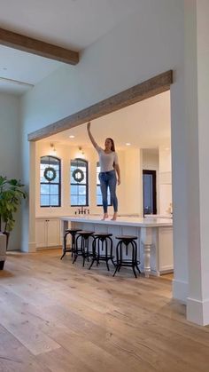 a woman standing on top of a kitchen island in a room with two stools