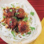 some meatballs and noodles are on a white plate next to a yellow napkin with a green leafy garnish