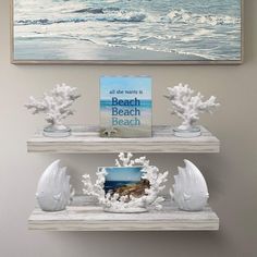 two white shelves with sea shells on them in front of a painting and an ocean scene