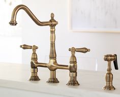 two faucets on a white counter top in a room with a painting behind them