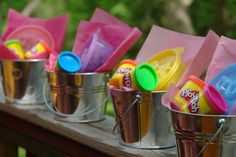 three buckets filled with play doh on top of a wooden table next to trees