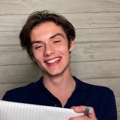 a young man smiles while holding a piece of paper