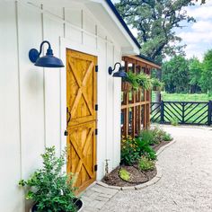 a small white shed with wooden doors and two planters on the front porch area