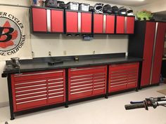 a garage with lots of red cabinets and tools on the counter top in front of it