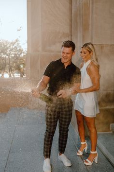 a man standing next to a woman in front of a building while spraying water on her face