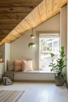 a window seat with pillows and plants on the windowsill in a room that has wooden ceilings