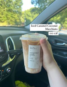 someone holding up a cup of iced caramel coconut macchiato in their car