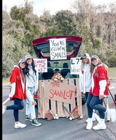 three girls are posing in front of the trunk of a car with their belongings and signs