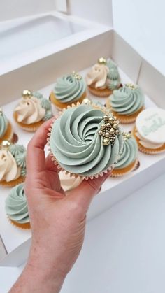 a hand is holding a cupcake with frosting and gold decorations on it in a box