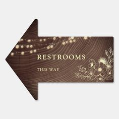 an arrow sign that says restrooms, this way with lights on it and flowers in the background