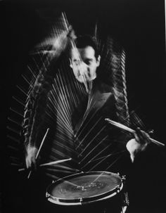 a man playing drums in front of a black and white photo with lines on it