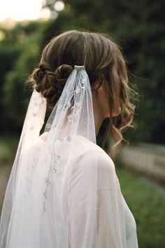 a woman wearing a veil and wedding dress in the sun with her hair pulled back