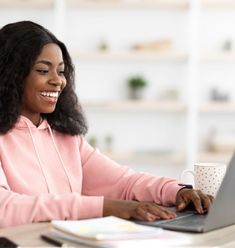 a woman sitting at a table with a laptop computer in front of her, smiling