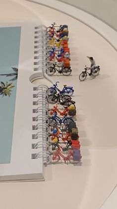 several small figurines are placed next to a spiral - bound notebook with an image of a man on a bike