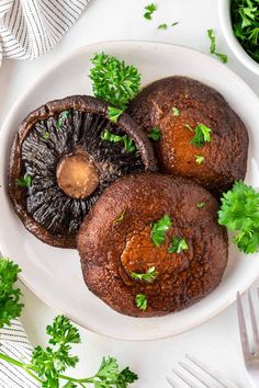 three mushrooms on a white plate with parsley around them and some silverware next to it