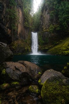 a large waterfall in the middle of a forest with moss growing on it's sides