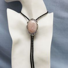 This pretty piece of rose quartz is mounted into a lightly ornate silvertone setting. It has a feminine air.   The bolo slide is set onto a 36 inch long braided black leatherette or leather  string tie with silverplated metal end caps. This is new, never worn, made in our very own Montana Rock shop, Rockin' JK Designs. Because these are natural stones, the color will vary between a soft pale pink and a medium pink.    The bolo slide measures 2 1/4 inches tall by 1 1/2 inches wide.  It will arriv Handmade Elegant Bolo Ties As A Gift, Handmade Elegant Bolo Ties For Gift, Elegant Adjustable Bolo Ties For Formal Occasions, Adjustable Elegant Bolo Ties For Formal Occasions, Elegant Silver Bolo Ties As A Gift, Elegant Silver Bolo Tie As Gift, Elegant Adjustable Bolo Tie As A Gift, Silver Bohemian Bolo Tie With Adjustable Cord, Bolo Ties