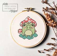 a cross stitch frog with a mushroom hat on it's head