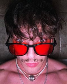 a shirtless man wearing red sunglasses and chain around his neck is looking at the camera