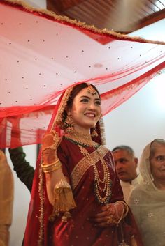 a woman in a red and gold bridal outfit smiles as she walks down the aisle