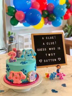 there is a cake on the table with balloons in the background and a sign that says, a clue a gliee guess who is two?