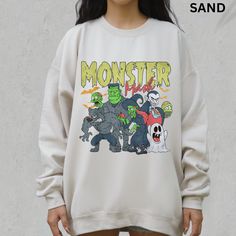 a woman standing in front of a wall wearing a white sweatshirt with monsters on it