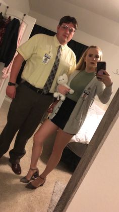 a man standing next to a woman holding a teddy bear in front of a mirror