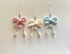 three crocheted bows hanging from hooks on a white surface with pearls and beads