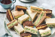 there are many sandwiches on the plate next to a cup of tea