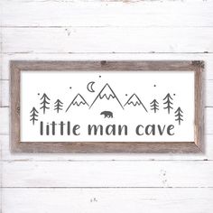 a sign that says little man cave with trees and mountains in the background on a white wooden wall