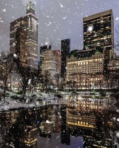 the city is lit up at night with snow falling