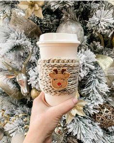 someone holding up a coffee cup in front of a christmas tree with ornaments on it