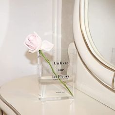 a single pink rose in a clear vase on a white table next to a mirror