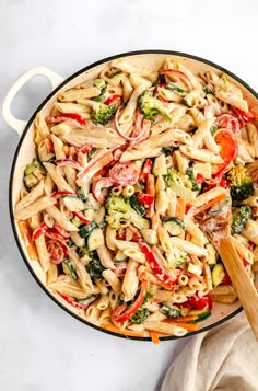 a skillet filled with pasta and vegetables on top of a white counter next to a wooden spatula