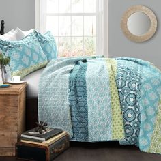 a bed with blue and green bedspread in a bedroom next to a window