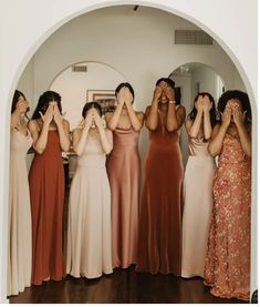 four women in long dresses are covering their eyes with their hands while looking into the mirror