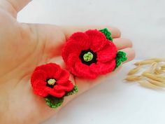 two crocheted red flowers are sitting on someone's hand next to oats