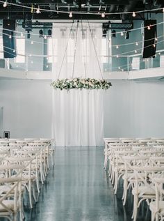 an empty room with white chairs and flowers hanging from the chandelier above them