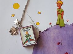 the little prince book necklace is laying on top of a piece of paper and has a small charm attached to it