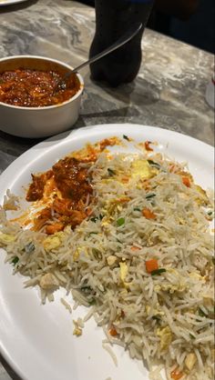 a white plate topped with rice and sauce next to a bowl of chili on a table