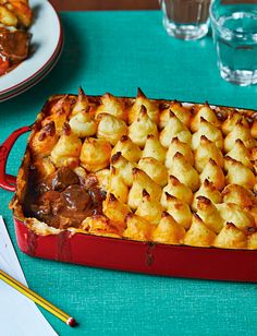 a red casserole dish filled with meat and potatoes on a green tablecloth