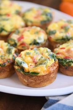 mini quiche cups with spinach and cheese on a white plate next to an orange